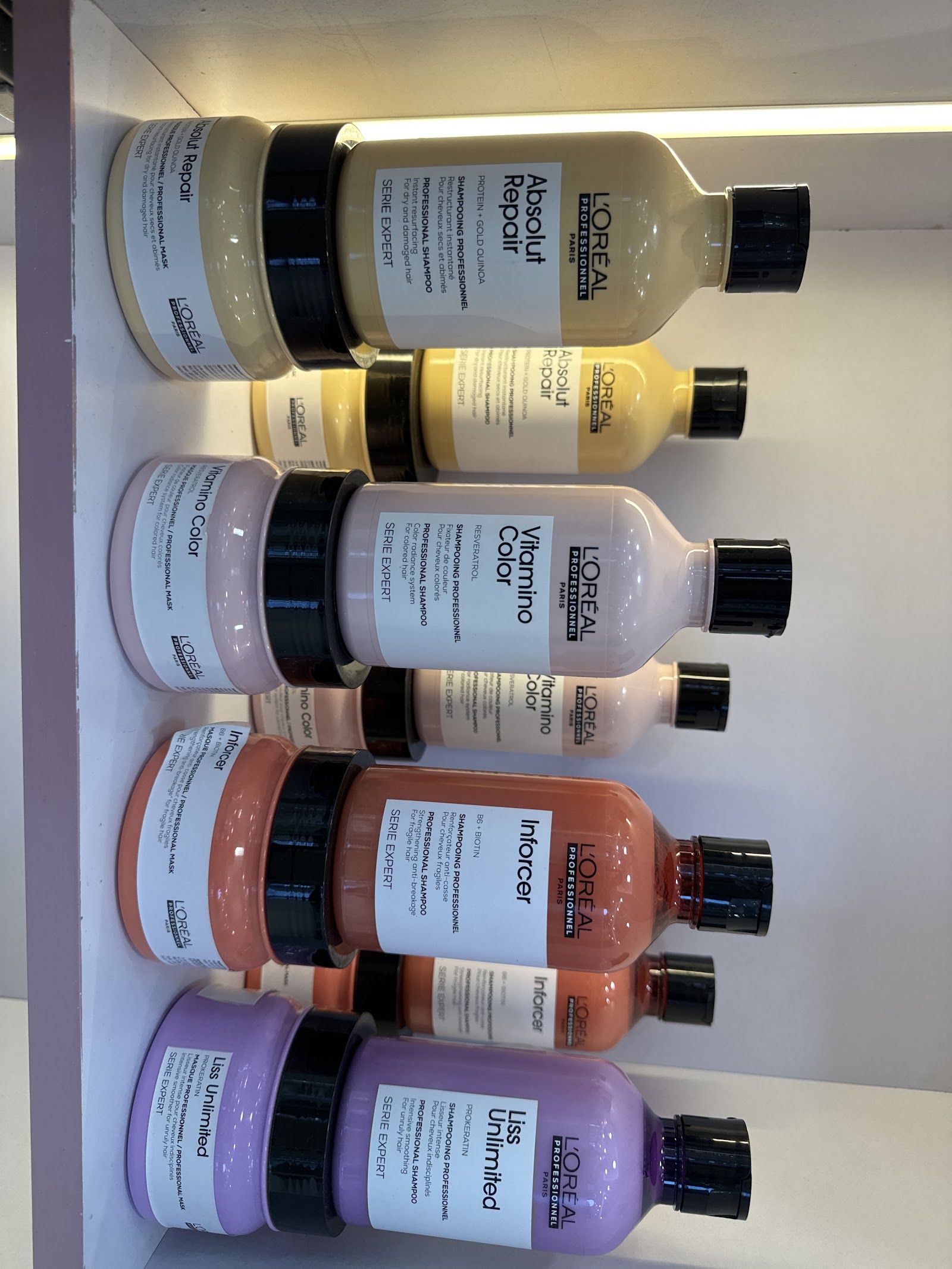 Back-lit shelf of L'Oréal Professionnel Absolut Repair, Vitamino Color, Inforcer and Liss Unlimited bottles.